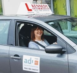 Rita Kennedy smiling at the wheel of the Kennedy School of Motoring car, with the Approved Driving Instructor sticker on the door.